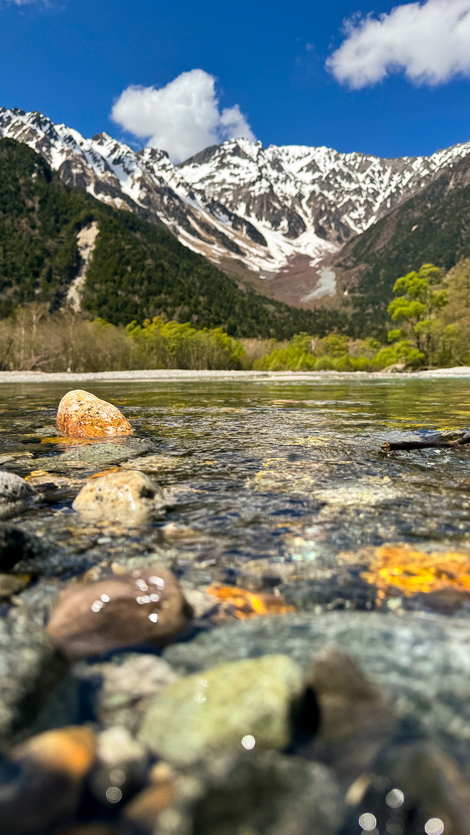 Clear alpine stream with moss-covered rocks and mountain peaks, Kamikochi hiking